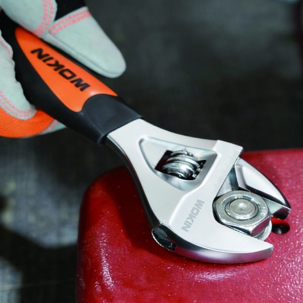 Gloved hand using a WOKIN stubby adjustable wrench to tighten a nut on a red metal surface.