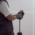 Person operating WOKIN 3D Laser Level on tripod with visible green laser lines for precise wall alignment in construction work