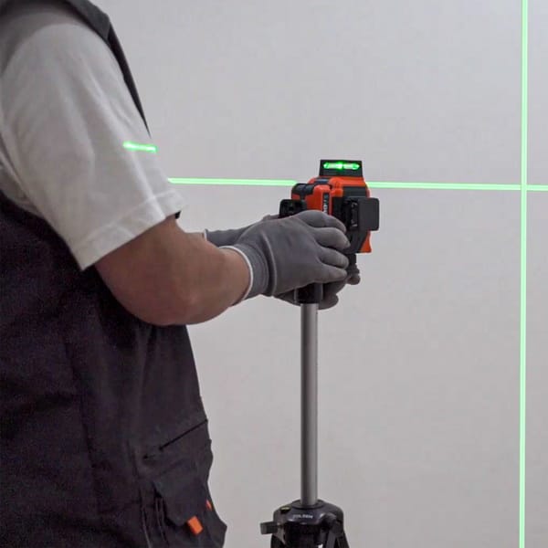 Person operating WOKIN 3D Laser Level on tripod with visible green laser lines for precise wall alignment in construction work